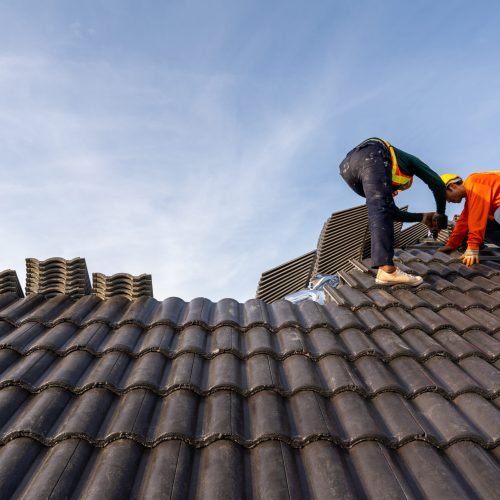 2 Roofers worker in protective uniform wear and gloves, using air or pneumatic nail gun and installing Concrete Roof Tiles on top of the new roof,Concept of residential building under construction.