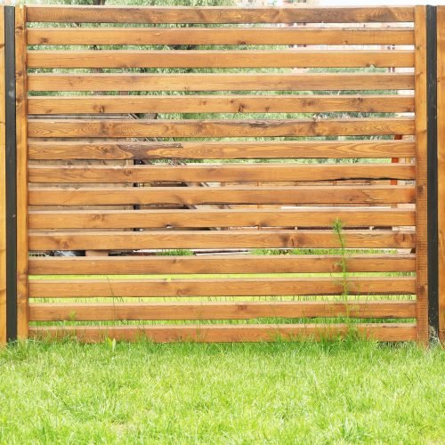 Background and texture of the fence of wooden planks covered with wood stain and green lawn.