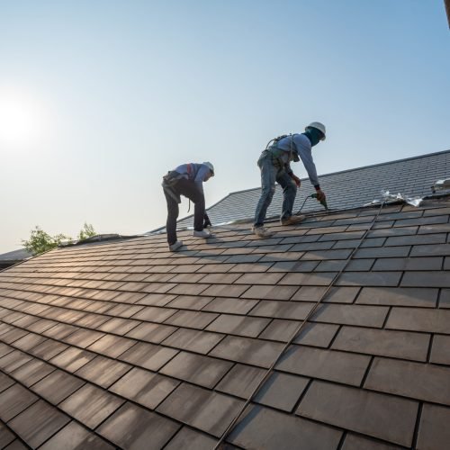 Roofer working in special protective work wear gloves, using air or pneumatic nail gun repair and replace roofing tiles on top of the new roof under construction residential building